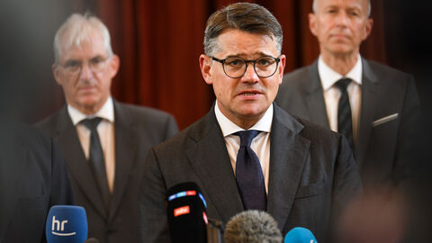 Ministerpräsident Boris Rhein steht, flankiert von anderen Menschen, vor Mikrofonen diverser Medien.