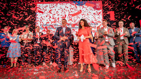 Mehrere Menschen stehen auf einer Bühne und es regnet rotes Konfetti.