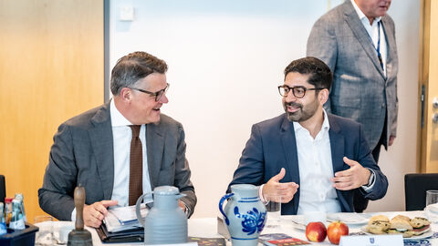 Zwei Männer sitzen nebeneinander an einem Tisch und reden miteinander.