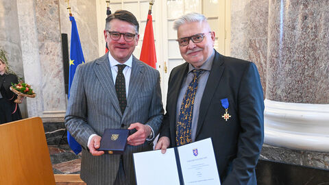 Zwei Männer stehen nebeneinander und halten eine Urkunde hoch.