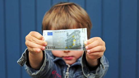 Kleines Kind streckt einen 5-Euro-Schein Richtung Kamera.