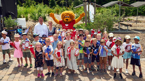 Eine Gruppe Kinder, die gemeinsam mit einem Löwen und Ministerpräsident Boris Rhein freudig in die Kamera schauen