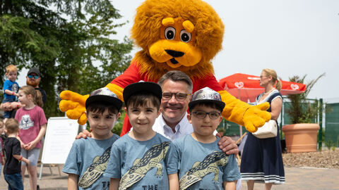 Ministerpräsident Rhein mit drei Drillings-Jungen, im Hintergrund der Hessen-Löwe als Maskottchen.